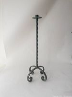Full view of the large dark iron floor candle holder with twisted central rod and curled feet base on a white background.