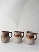 Three large Laurentian Tundra earthenware mugs with brown upper glaze and beige lower portion with drip design, arranged side by side.