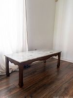 Side view of marble top coffee table showing the wood base and legs on a wood floor near a curtain.