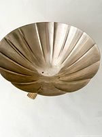 Front angled view of a fluted, vintage metal fruit bowl showing the bowl's stainless steel texture and brass legs.