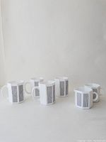 Four octagonal milk glass mugs and two creamers arranged together, showing their white milk glass with black stripe patterns.