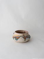 Front side view of the Nemadji pottery hanging planter showing blue and orange glaze streaks on beige pottery surface with metal hooks for hanging.