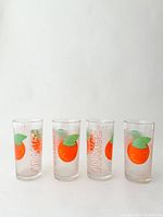 Four clear vintage juice glasses with bright orange and green fruit graphics and 'ORANGE' text on each.
