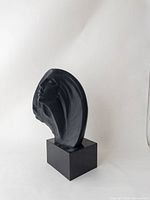 Front-left angled view of the black Austin Productions Stargazer sculpture showing stylized female face and flowing hair on black rectangular base.