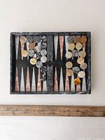 Top view of the rectangular stone backgammon board with stone checkers arranged on the points, showing the marbled color pattern of the board and pieces.