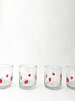 Four clear hand blown glass tumblers decorated with small red strawberry designs spaced around the glass.