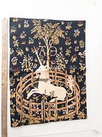 Front view of tapestry showing detailed unicorn design with floral and tree embroidery on black background with wooden ruler for scale.