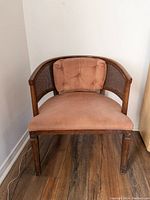 Front view of the vintage cane chair with light pink upholstery and tufted back cushion.