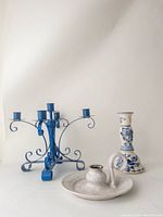 Photo showing blue metal 5-arm candelabra, white ceramic candle holder with handle and a white and blue ceramic candle holder with floral design from side angle.