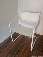 Front angled view of white tubular chair with white leather seat and backrest against wall with wood flooring.
