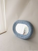 Full view of light blue wicker mirror placed against a white wall.