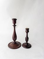 Two turned dark wood candle sticks of different heights on a white background.