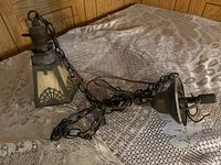 Antique hanging light fixture lying on a lace tablecloth, showing the metal chain, metal frame, and cream glass shade with black decorative pattern