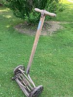 Full view of the antique reel hand mower showing wooden handle, metal frame, and cutting reel with wheels on grassy background.