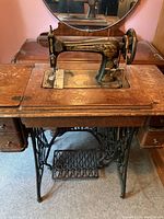 Full frontal view showing the vintage Singer sewing machine mounted in a wooden treadle table with iron pedal base and drawers on the sides.