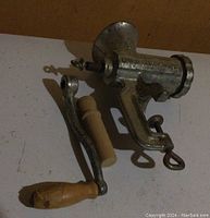 Side view showing detached wooden handle and main cast iron grinder body on a flat surface