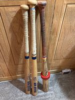 Photo showing all three wooden baseball bats standing against a wooden cabinet, wrapped handles visible, varying finish and colors.