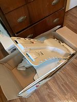 Photo of the Bellavita bathlift in a cardboard box showing the seat, partially folded with white plastic and metal frame parts visible.