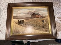 Photo of framed countryside print showing horse and buggy near farmhouse, in wood and gold frame.