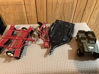 Overview of the full lot including the green army jeep, metal disc plow, trailer, and farm attachment lined up on a fabric surface.