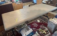 Full view of the beige folding plastic table in a room environment over a patterned rug.