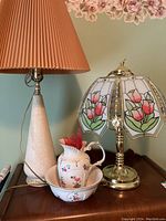Wide shot showing two table lamps side by side and the ceramic jug and basin on a wooden surface under floral wallpaper