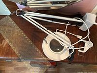 Photo showing the magnifier lamp with articulated arm and clamp base next to a clear plastic ruler with yellow markings laid on a wooden table.