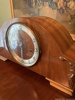 Front view of retro wooden mantle clock on a wooden surface with visible glass clock face and carved wood details.