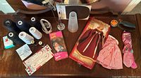 Full lot on wooden table including threads, needles, doll forms, patterns, rotary cutter, and doll dresses.