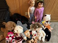 Image showing various vintage stuffed animals and dolls arranged on the floor with two standing baby dolls in the background.