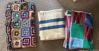 Three folded blankets pictured: two crocheted afghans with colorful square patterns and one cream wool blanket with blue stripes.