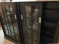 Two black bookcases with grid design sliding glass doors, partially opened to show adjustable shelves inside.