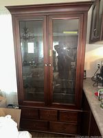 Full front view of the dark wooden cabinet with two glass doors and drawers below.