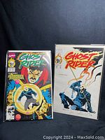 Two Ghost Rider comics side by side on black background, both in protective sleeves, signed on the covers.
