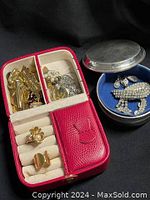 Photo of red jewelry box open showing assorted gold-tone jewelry including chains, brooches, and rings.