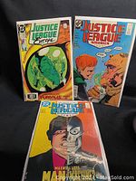 Three Justice League comic books positioned to show front covers: Justice League Europe, America, and International.