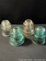 4 antique glass insulators with varying shapes and colors, some with embossed markings