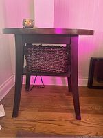 View of one dark wood end table featuring round top and woven basket shelf holding small decorative items. Shows legs and basket fit.