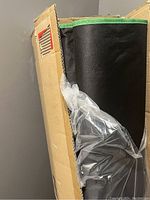 Partially unpacked black fabric grow tent with green trim inside cardboard box.