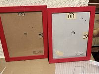 Back view of two red photo frames showing clips and mounting hardware