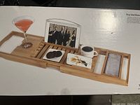 Bamboo bath caddy displayed with compartments holding a glass, phone, soap, and a cup.