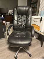Front view of a black leather computer desk chair showing padded seat, ruched backrest, armrests, and metal base with wheels.