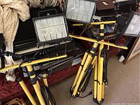 Photo showing three dual head construction lights mounted on yellow tripods, with cords coiled and attached. Equipment appears lightly used and functional.