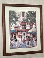 Framed art showing street café painting with people, umbrellas, trees, building, in brown wooden frame with white mat.