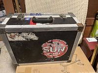 Black aluminum attaché case exterior with peeling stickers and black handle, showing wear and tear.