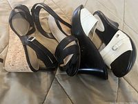 Photo showing two pairs of women's shoes: one pair of black Tommy Hilfiger slides and one pair of black Le Chateau wedge heels with cork wedge heel and ankle straps.