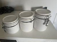 Three white ceramic kitchen storage canisters with metal latch sealed lids shown closed.