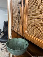 Side view of one hanging planter basket suspended by black metal chain from a cabinet.