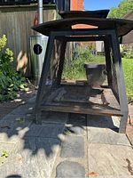 Outdoor metal fireplace sitting on stone patio, showing black metal with mesh sides and a pyramid top. Some light rust visible at base.