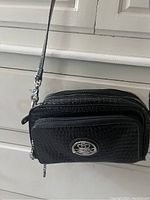 Black multi-pocket ladies handbag with textured crocodile pattern, silver emblem, multiple compartments, and detachable strap
